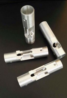 Vier silberne, zylindrische Metallteile mit Aussparungen, angeordnet auf dunklem Hintergrund.