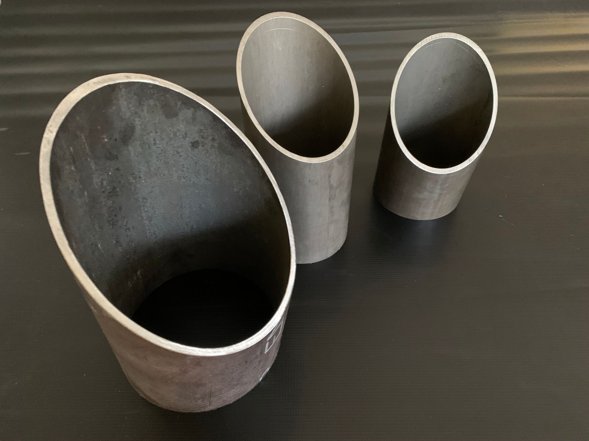 Zwei Metalldrahtschlaufenklemmen stehen aufrecht auf einer dunklen Oberfläche vor schwarzem Hintergrund.