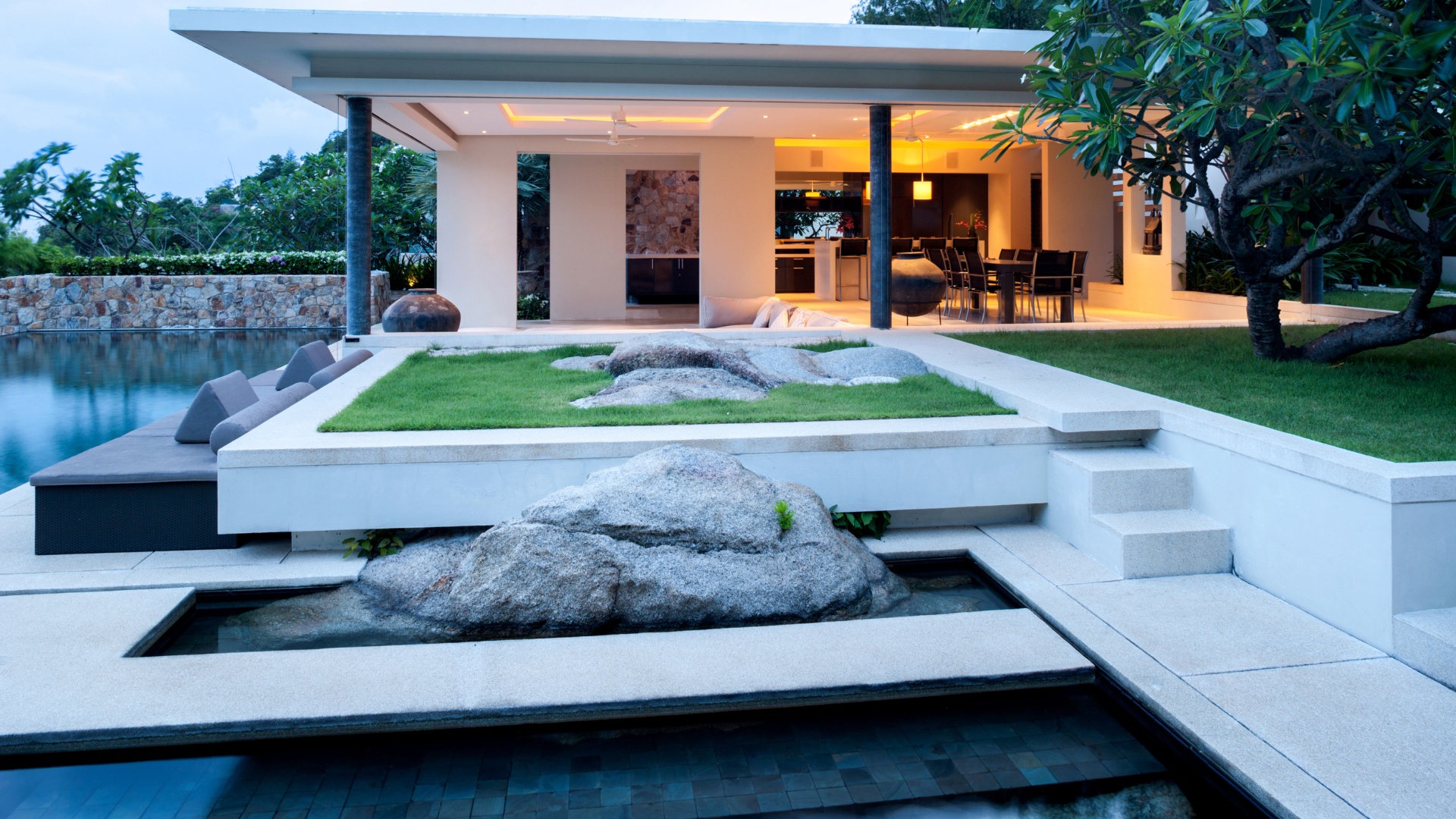 Une maison moderne minimaliste avec piscine, aménagement paysager en pierre et terrasse gazonnée au crépuscule.