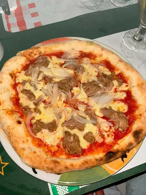 Una pizza con carne y queso en un plato sobre una mesa.