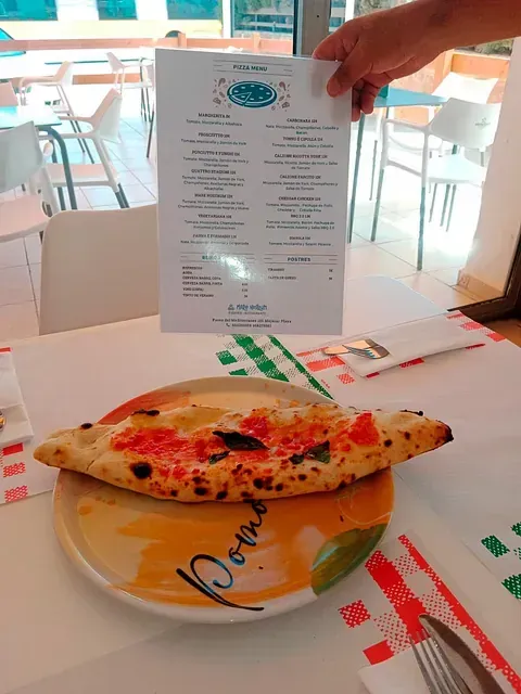 Una persona sostiene un menú sobre una pizza en un plato.