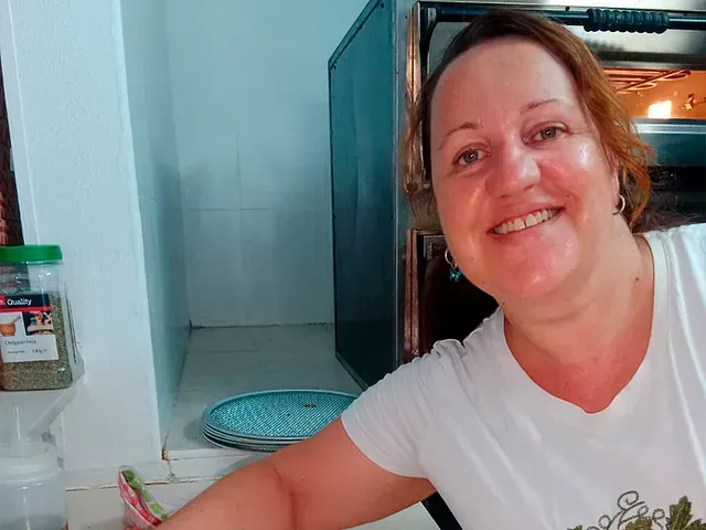 Una mujer sonríe delante de un horno en una cocina.