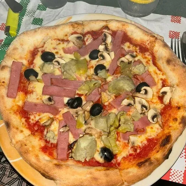Una pizza con jamón, champiñones y aceitunas en un plato.