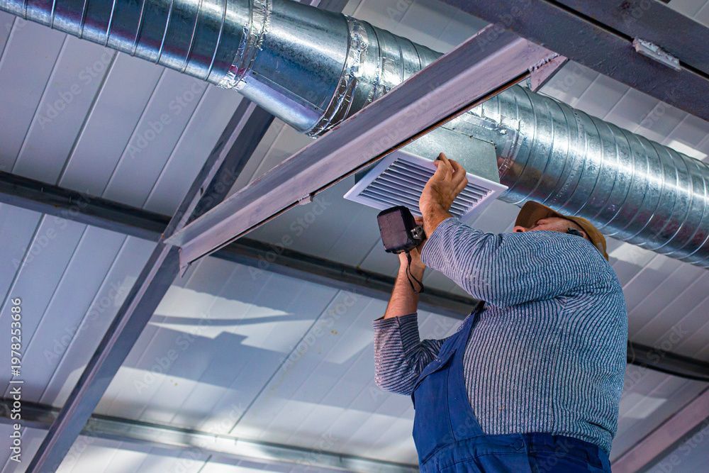 Techniker installiert oder überprüft Deckenlüftungskanäle mit einem Handwerkzeug in einem Industrieinnenraum