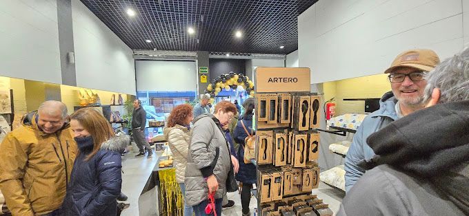 Un grupo de personas hojeando artículos en una tienda. A la derecha, un expositor de madera con cucharas. La gente observa la mercancía y conversa.
