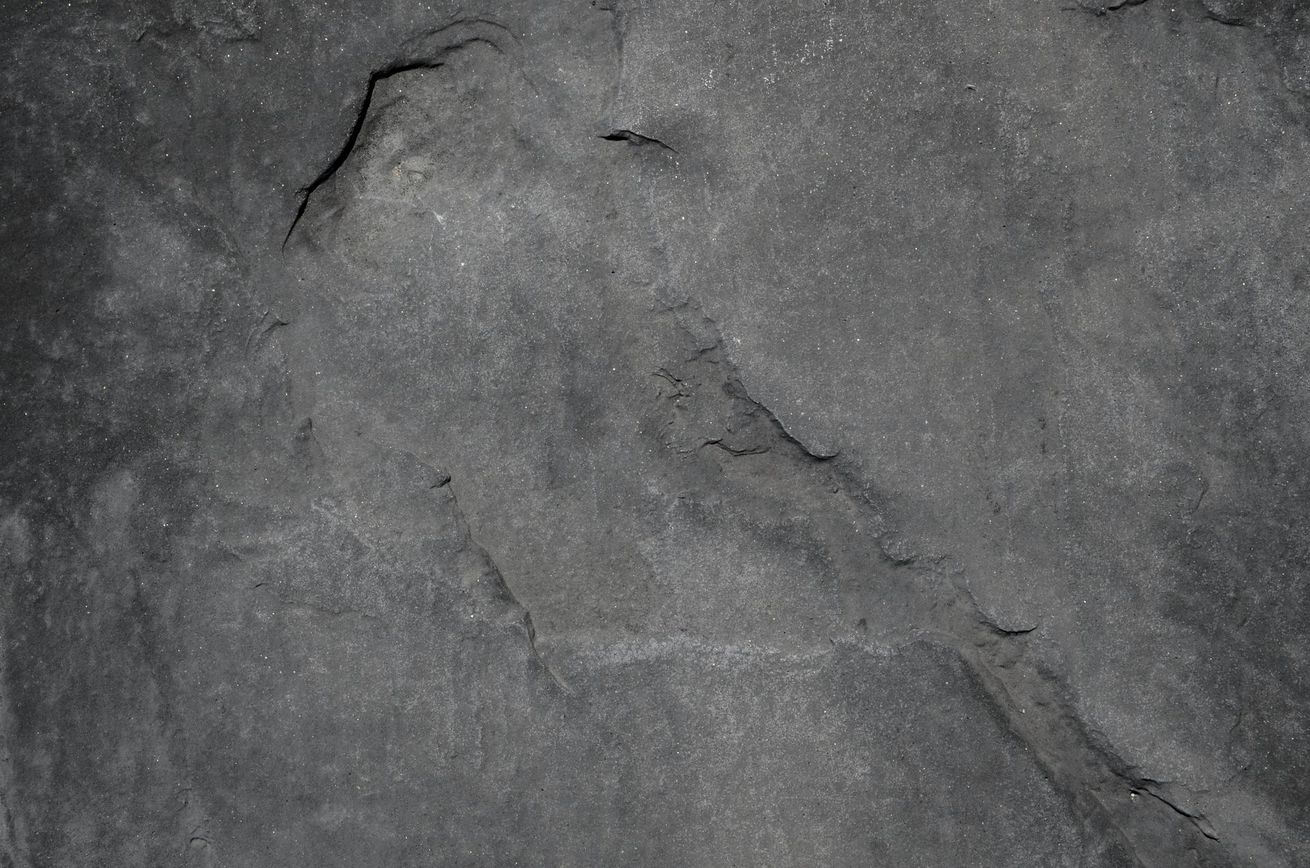 Superficie de piedra agrietada de color gris oscuro con textura rugosa.