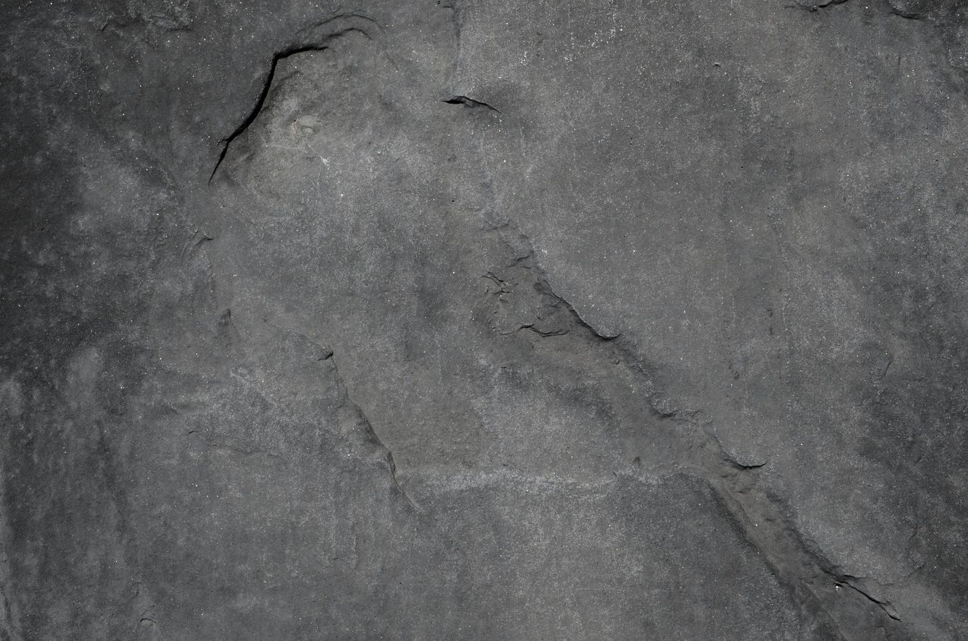 Superficie de piedra agrietada de color gris oscuro con textura rugosa.