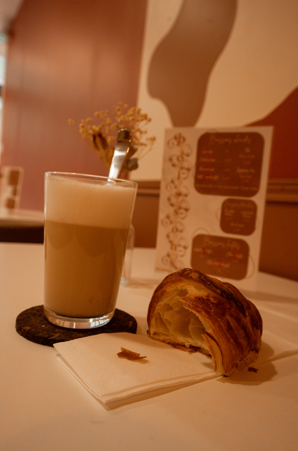 Un café latte à côté d'une pâtisserie sur une table blanche, avec une carte de desserts en arrière-plan.