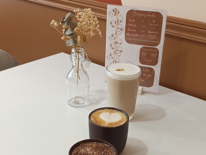 Deux cafés lattes, un vase avec des fleurs séchées  et une carte posés su sur une table.
