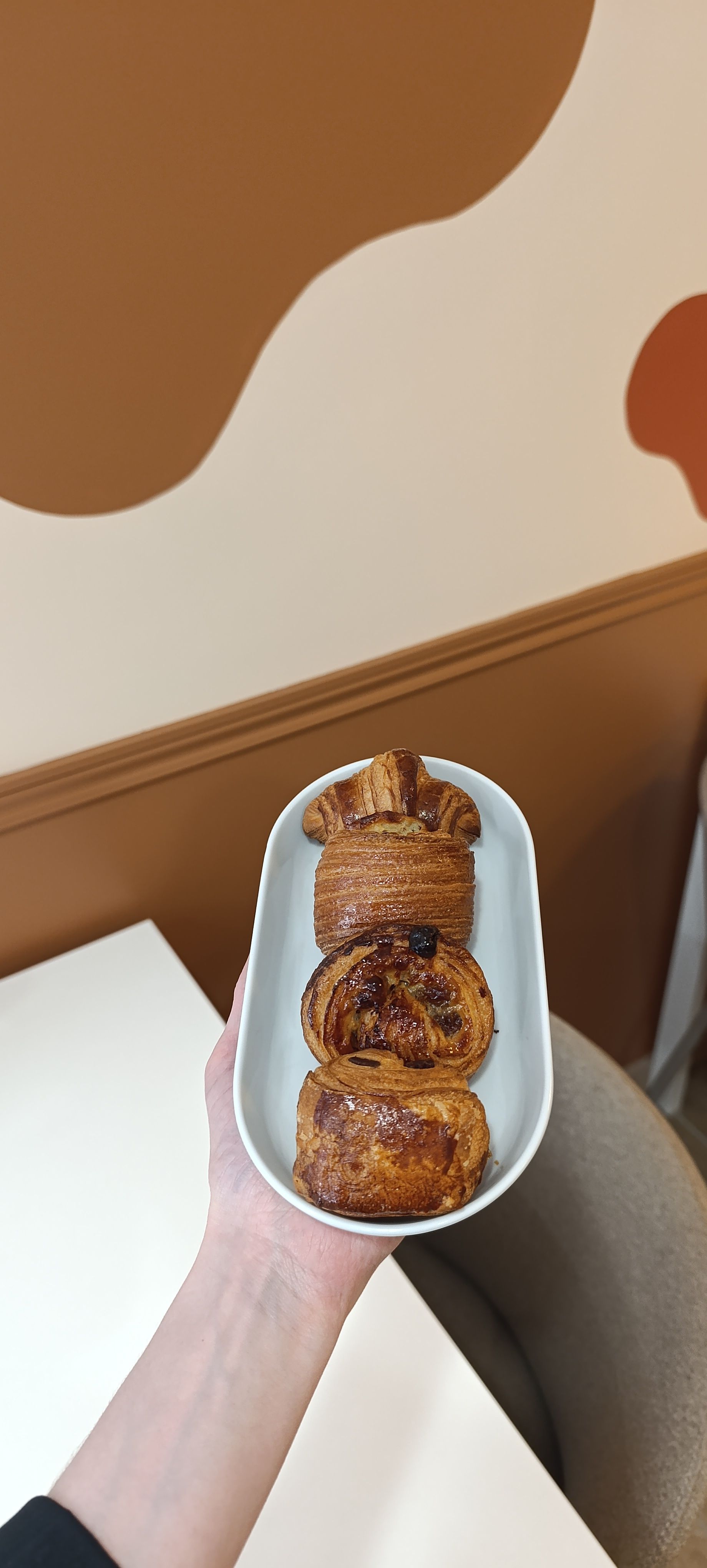 Une main tenant un petit plateau de viennoiseries devant un mur beige et marron