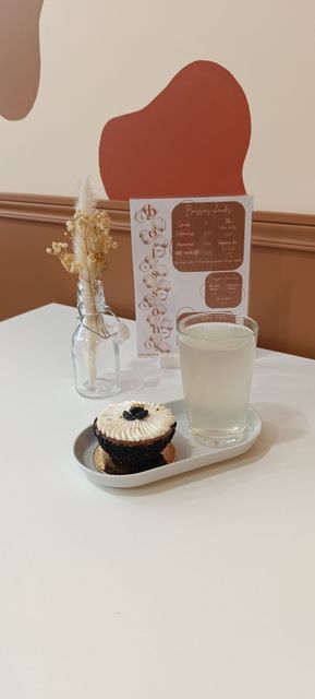 Dessert et boisson servis sur un plateau posé sur une table blanche, avec un vase de fleurs et une carte en arrière-plan.