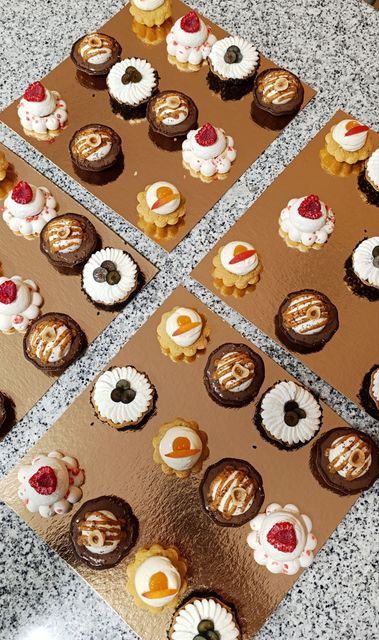 Assortiment de mini-pâtisseries décorées disposées en rangées sur des plateaux en carton doré.