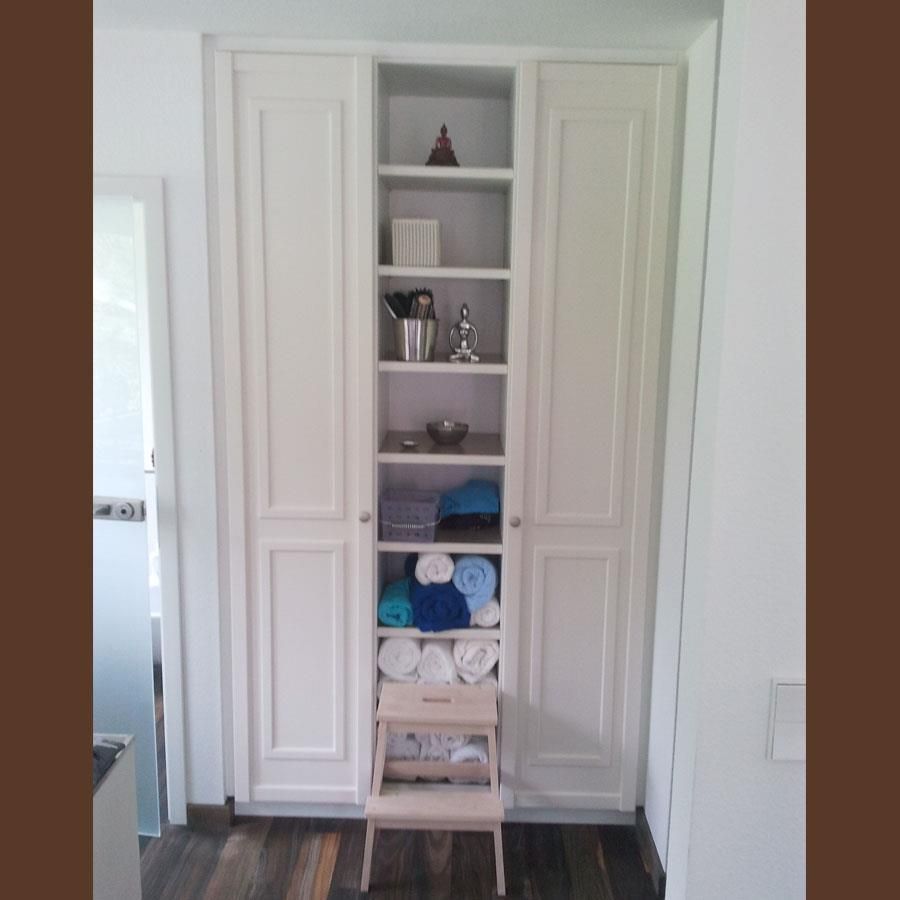 Ein weißer Schrank voller Handtücher und ein Hocker