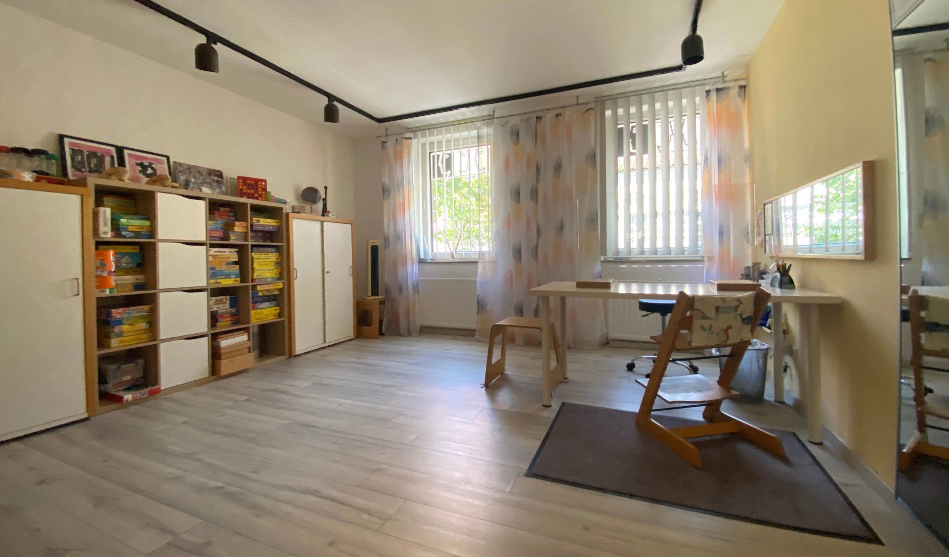 Helles Klassenzimmer mit Regalen, Tischen, Stühlen und Sonnenlicht durch hohe Fenster
