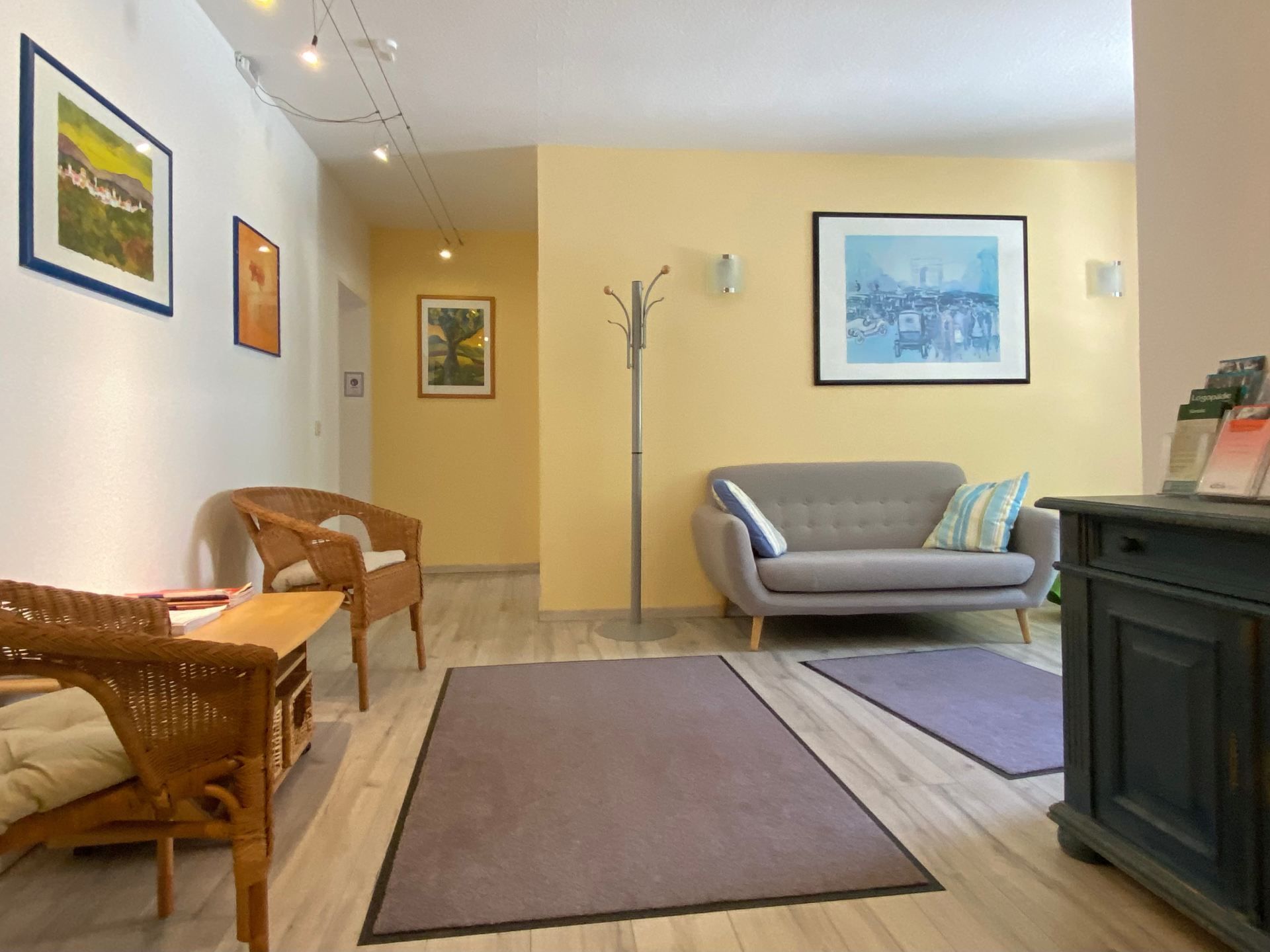 Helles Wohnzimmer mit Korbsesseln, grauem Sofa, Teppichen, gerahmten Bildern und einem schwarzen Schrank.