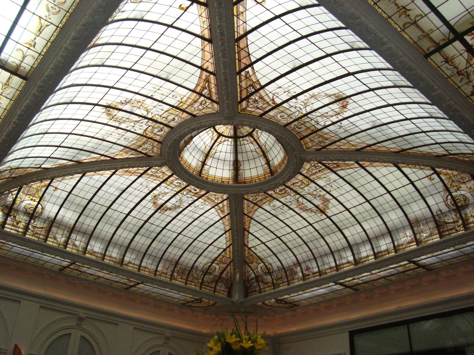 Plafond en verre orné de motifs circulaires et arqués, de touches dorées et d'une verrière.