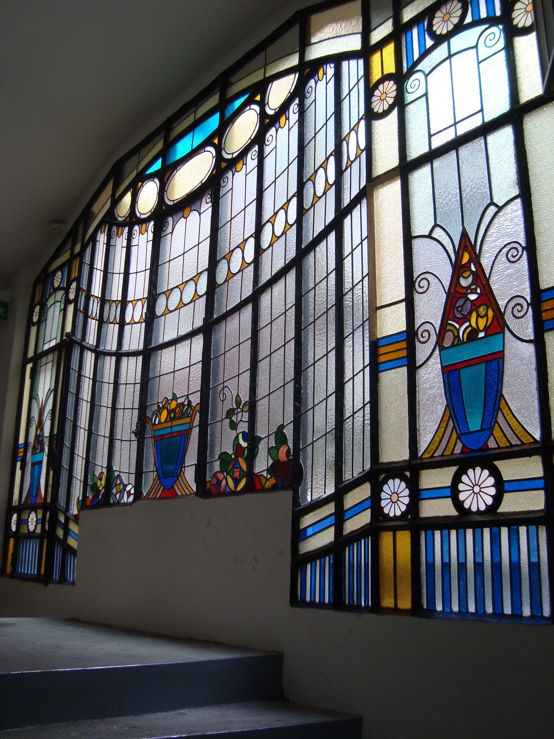 Vitrail à motifs géométriques bleus, jaunes et blancs au-dessus de l'escalier.