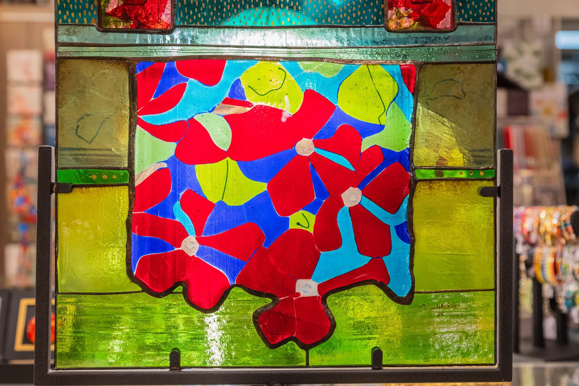 Panneau de vitrail à fleurs rouges sur fond bleu et vert, dans un cadre de galerie.