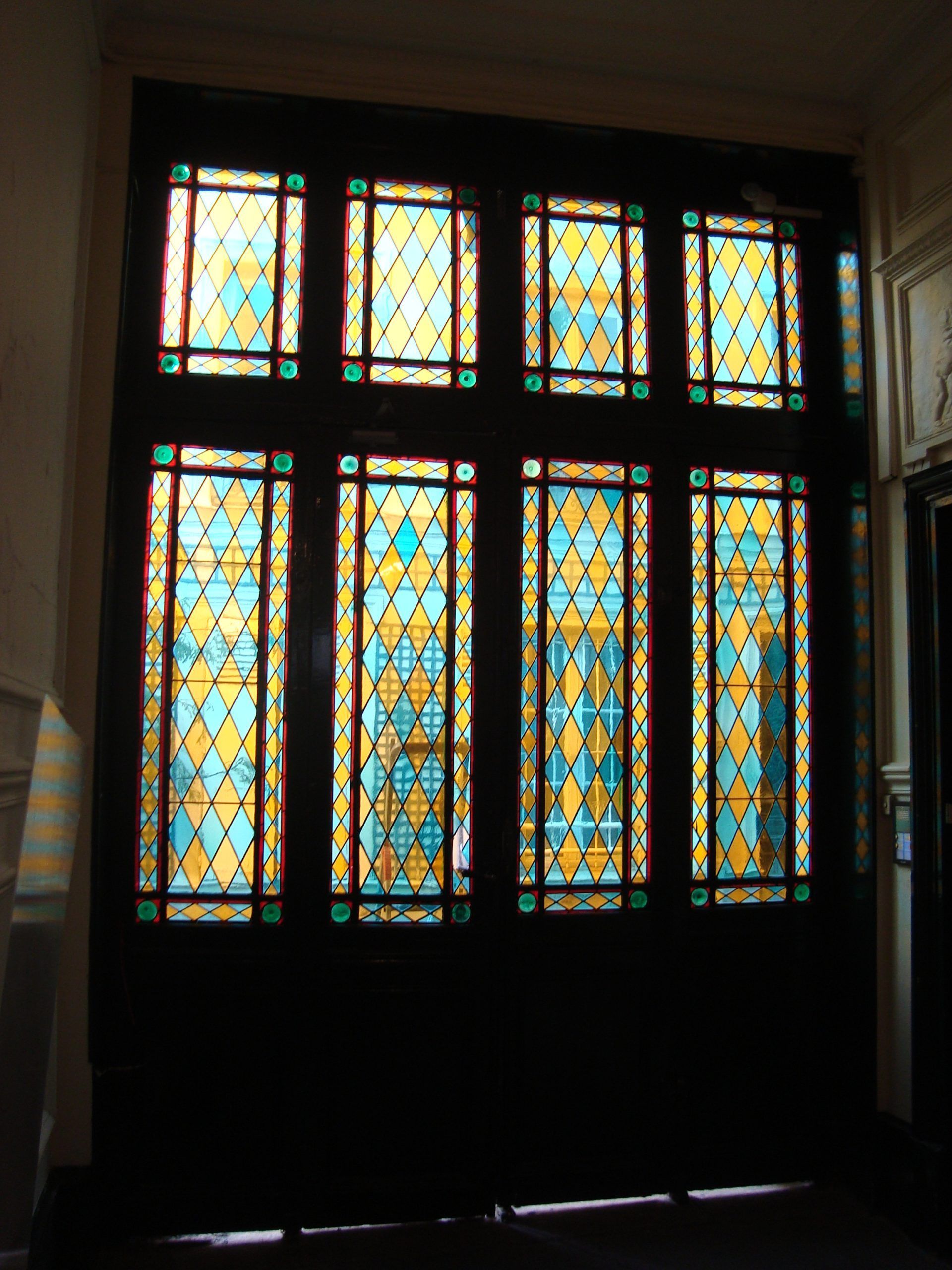 Vitrail à motif de losanges jaunes et turquoise, encadré d'un cadre en bois foncé.