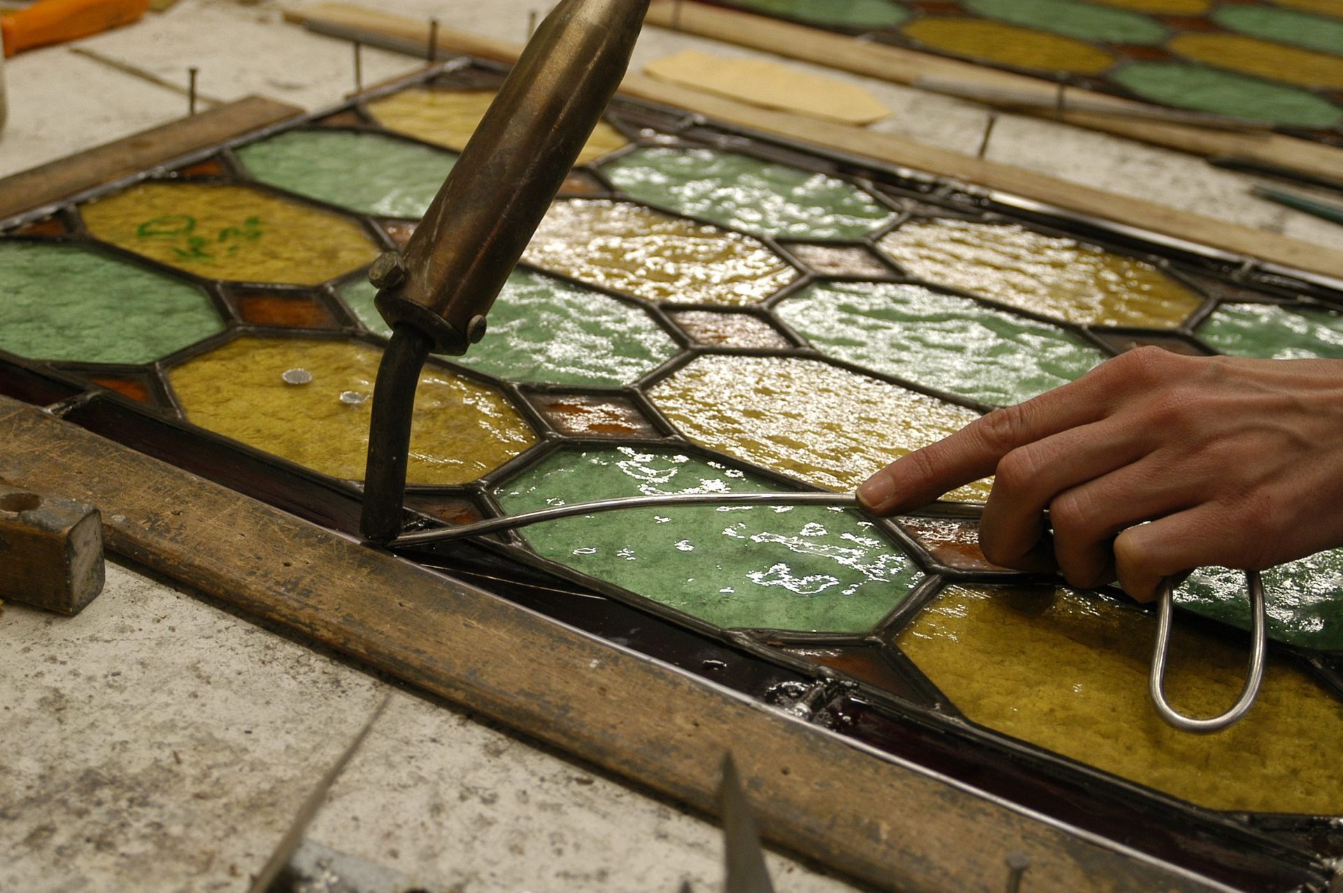 Une personne soude un vitrail au plomb à l'aide d'un fer chaud. On distingue différentes couleurs de verre.