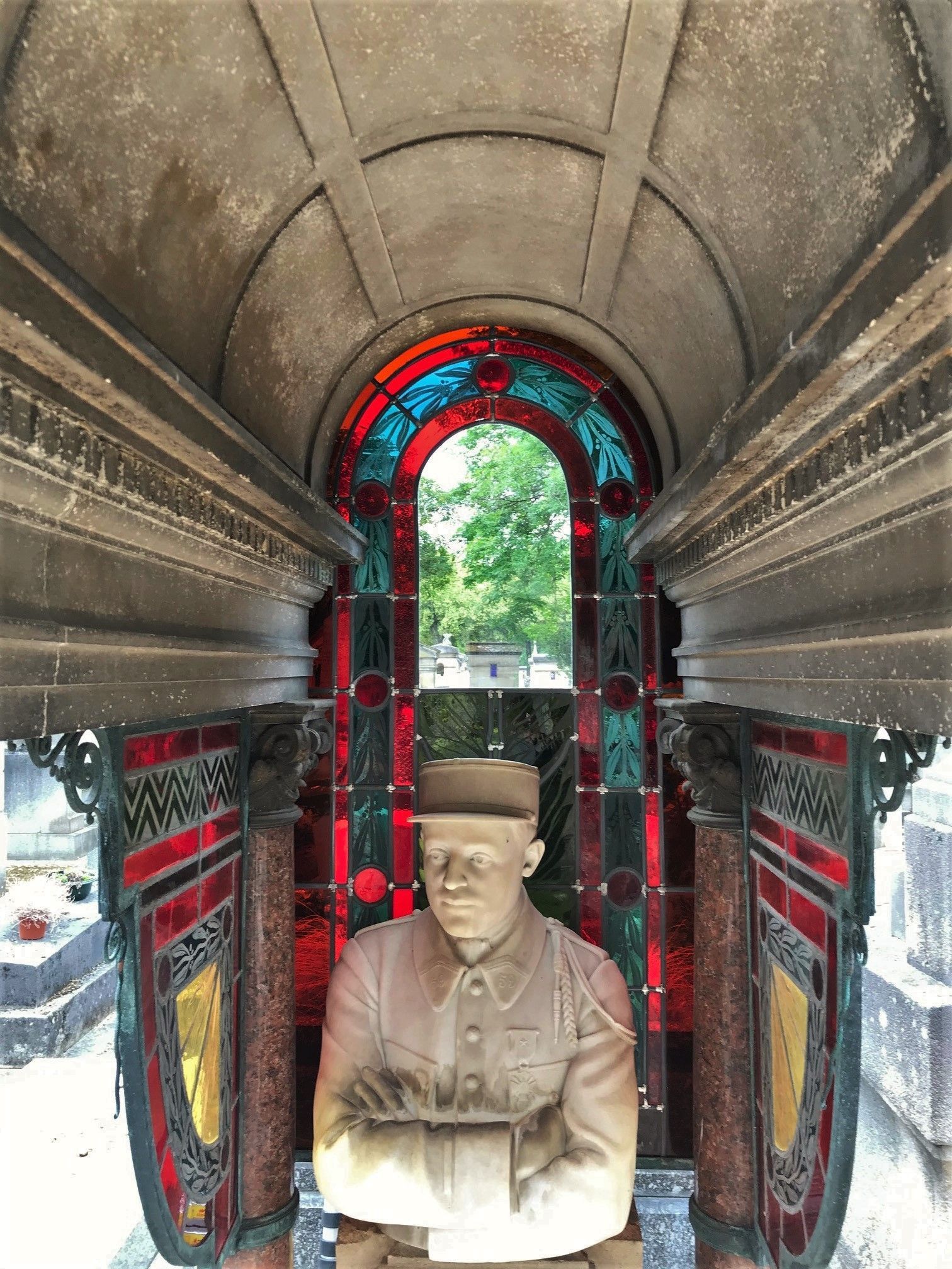 Statue d'un homme en uniforme militaire, dans une crypte ornée de vitraux.