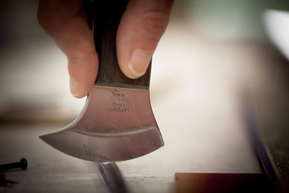 Main tenant un couteau à lame courbe, probablement pour le travail du cuir, en train de couper une surface.