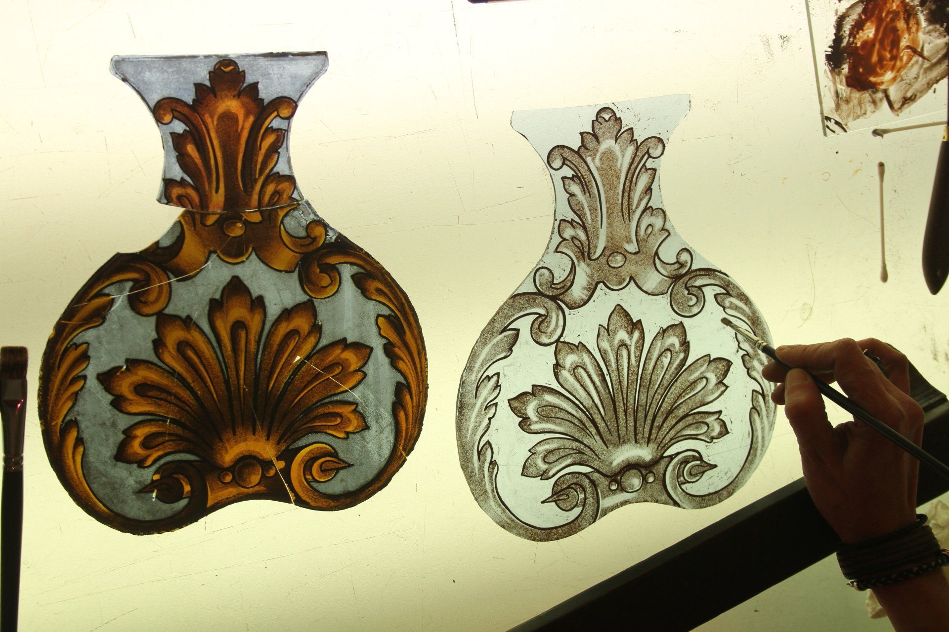 Des vases en vitrail, l'un doré, l'autre peint, comme une main qui utilise un pinceau.