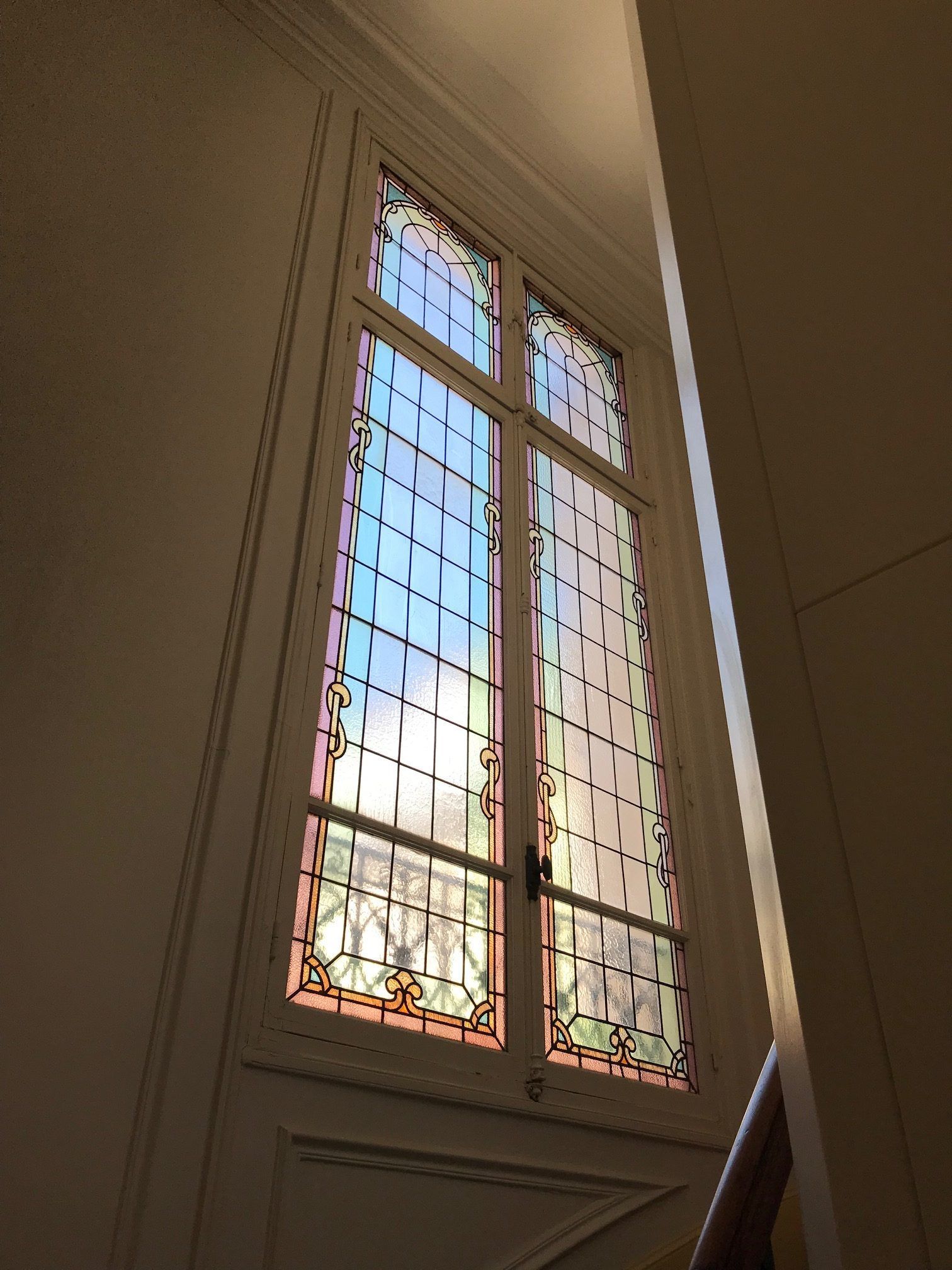 Grand vitrail rectangulaire à cadre blanc, sur un palier d'escalier.