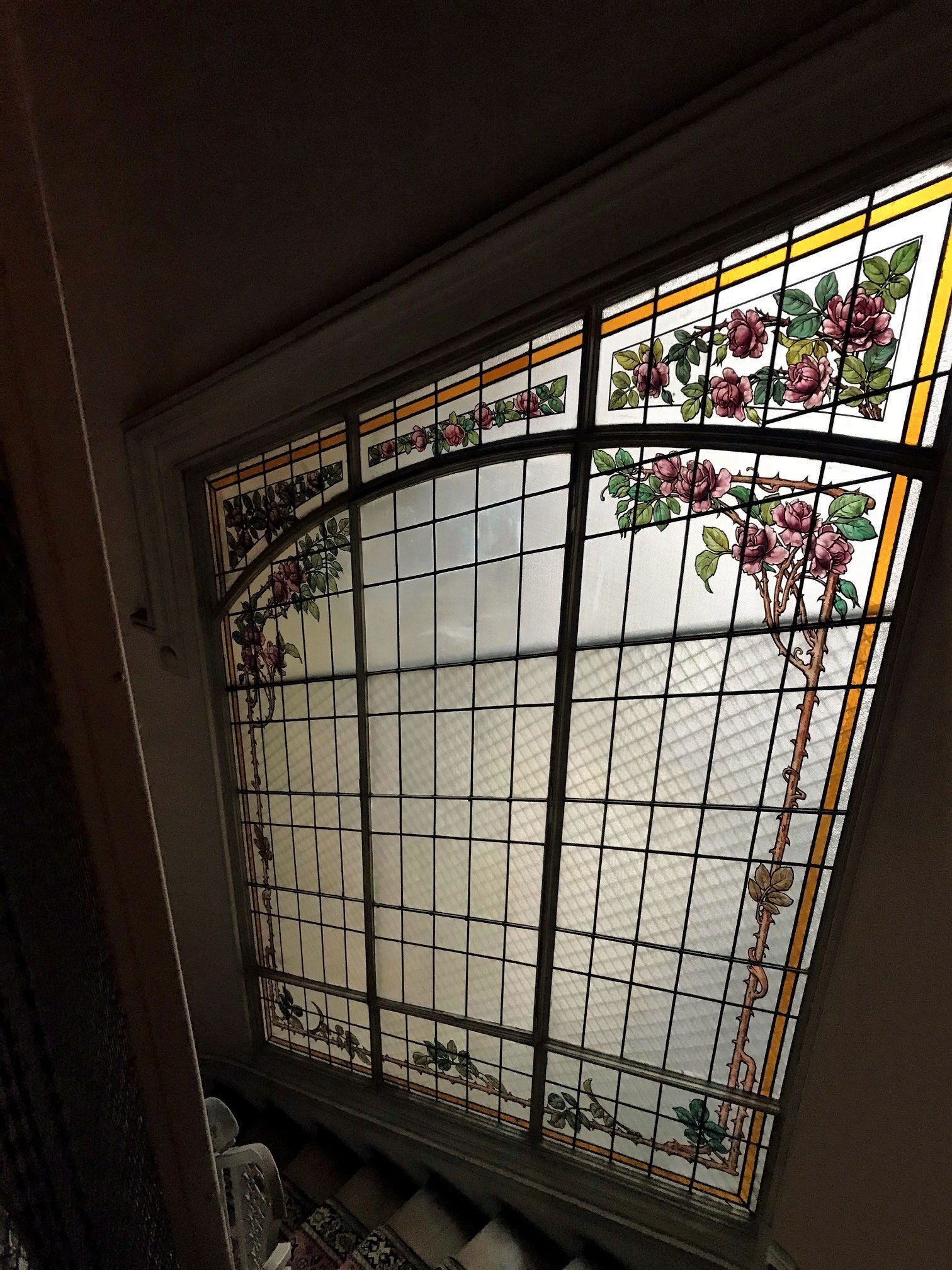 Puits de lumière en vitrail à décor floral : roses roses, feuilles vertes et bordures dorées. Vue d’en bas.