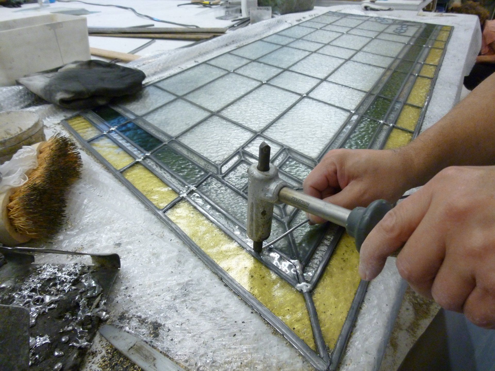 Personne utilisant un outil pour réparer un panneau de vitrail ; travail en cours, avec du verre coloré.