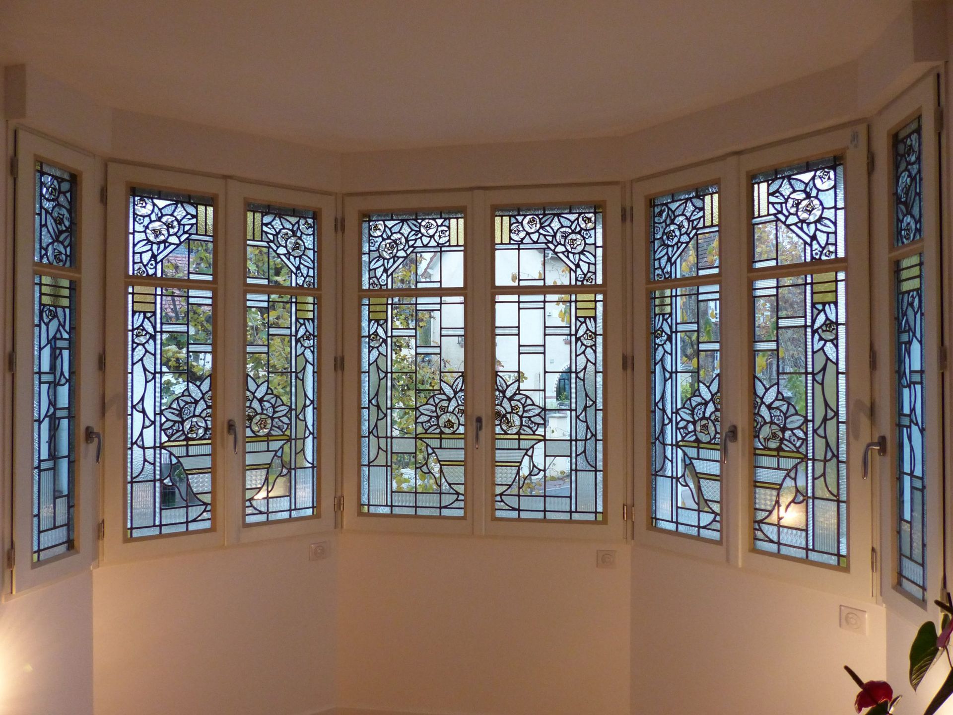 Baie vitrée ornée de vitraux, encadrements blancs, donnant sur un paysage urbain.