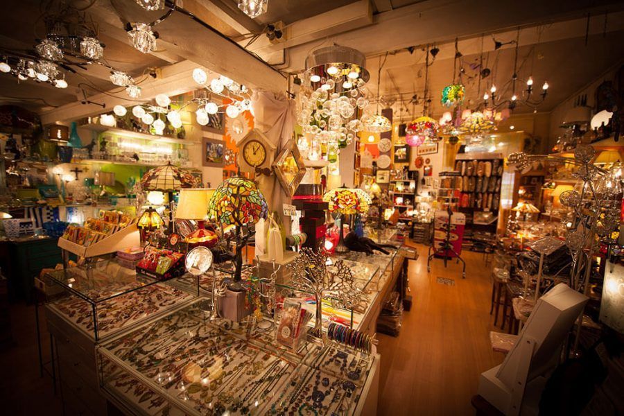L'intérieur d'une boutique encombrée de lampes et de bijoux, baignée d'une lumière vive, dans des tons chauds.
