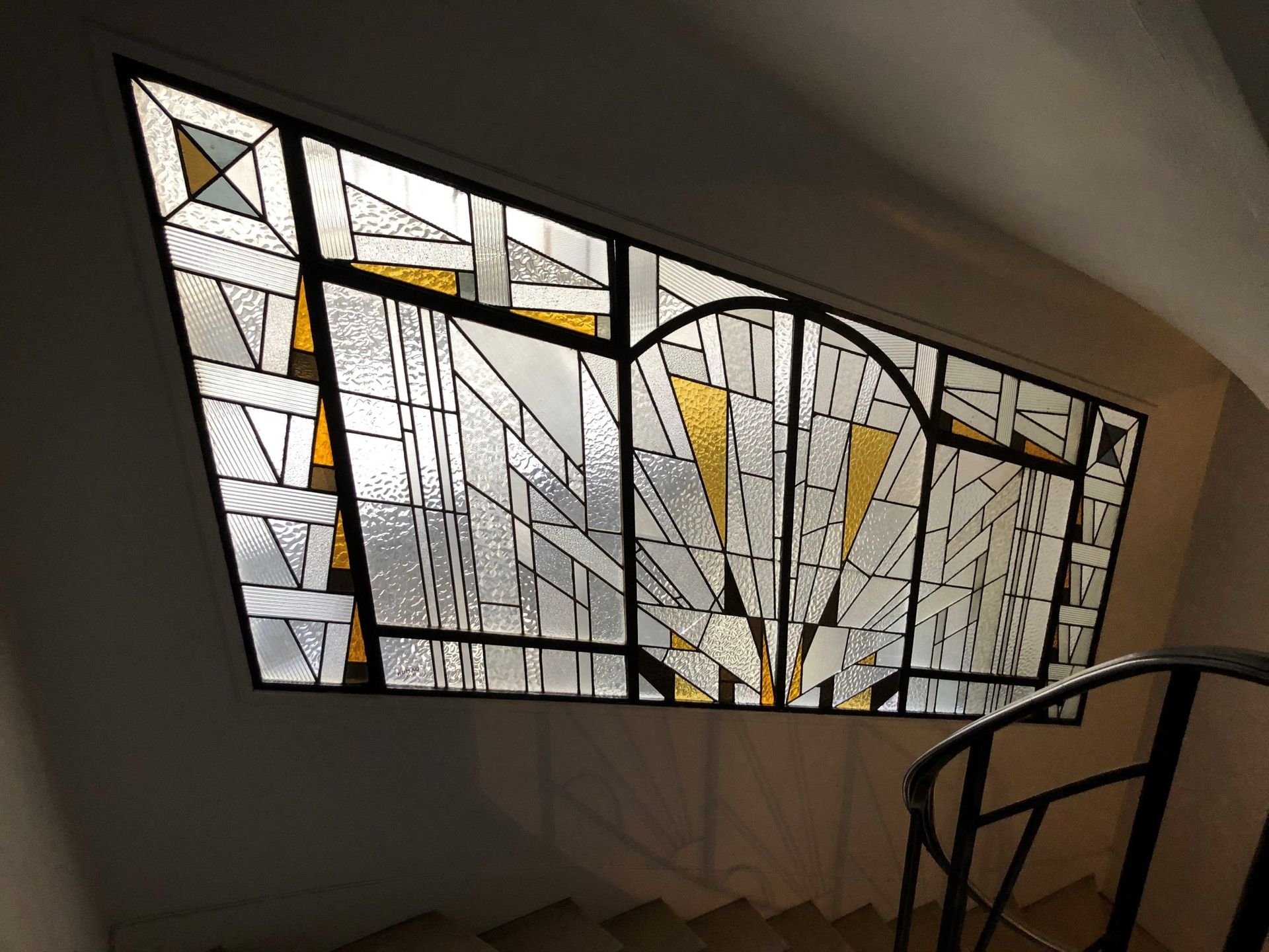 Vitrail à décor géométrique Art déco au-dessus d'un escalier descendant, en verre doré et transparent.