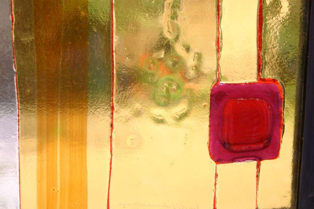 Vitrail orné d'un carré rouge et de formes abstraites dorées et vertes.