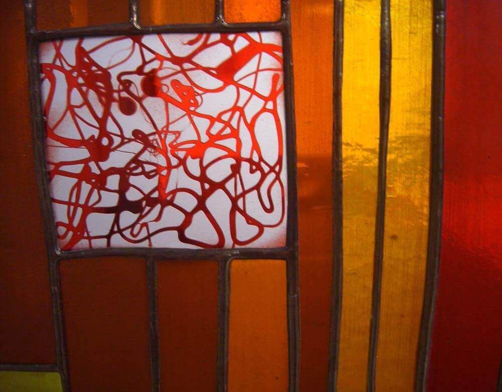 Panneau de vitrail représentant un carré blanc avec des éclaboussures de peinture rouge, à côté de panneaux de verre orange et jaune.