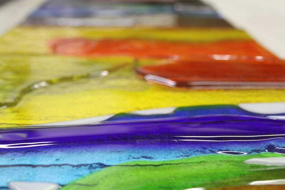 Gros plan sur une œuvre d'art en verre fusionné présentant des couches de couleurs vives de l'arc-en-ciel.