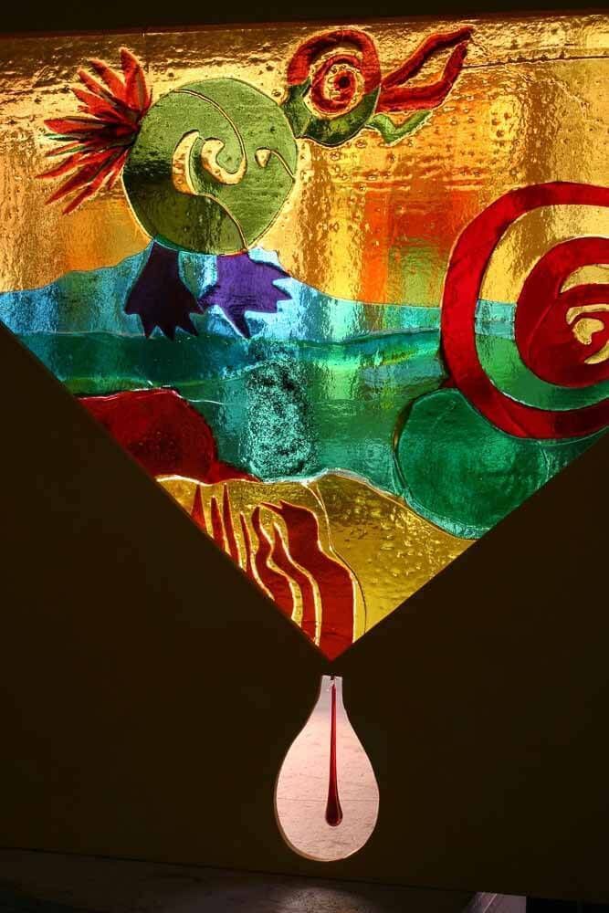 Objet d'art en verre coloré représentant un oiseau vert orné d'une spirale et d'une goutte en forme de larme, sur fond doré.