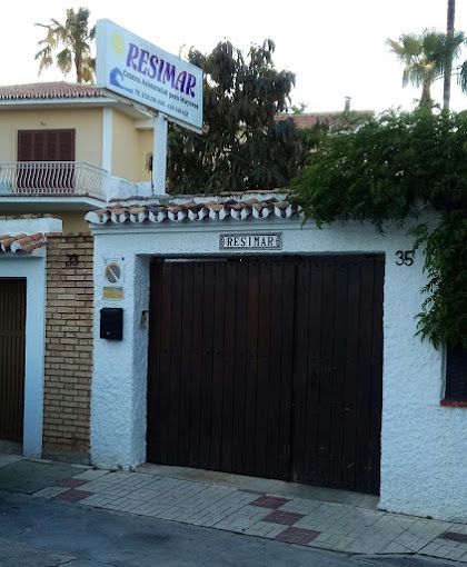 Edificio blanco con portón marrón, cartel 