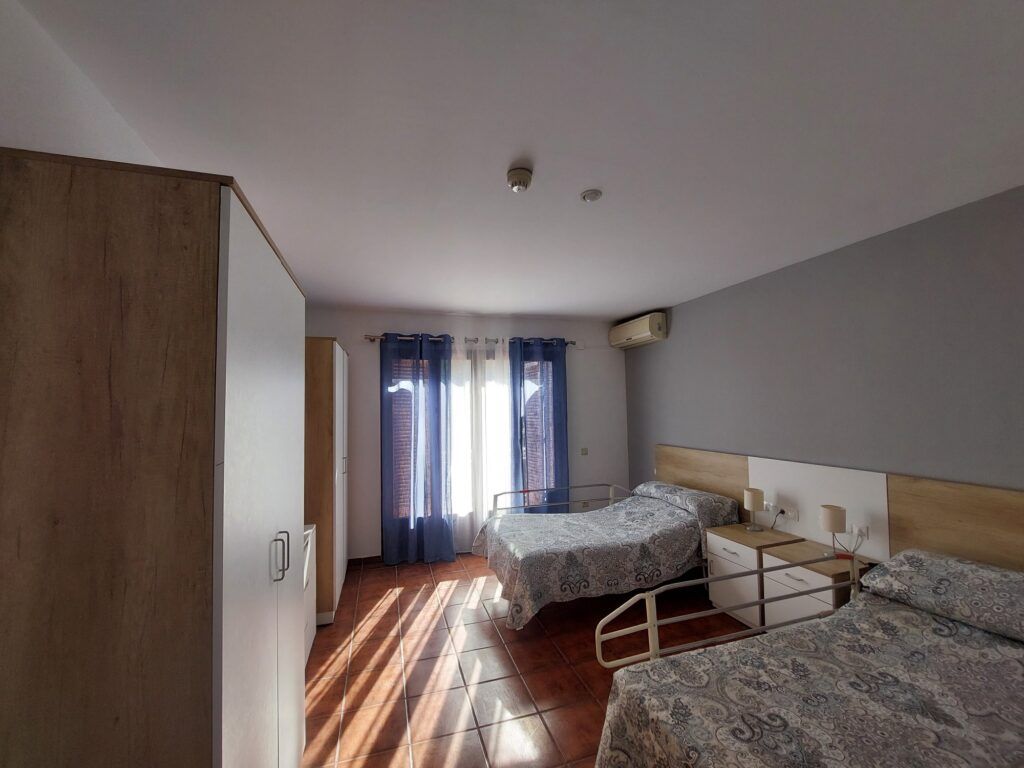 Dormitorio con dos camas, dos armarios y una ventana con cortinas azules; suelo de madera.