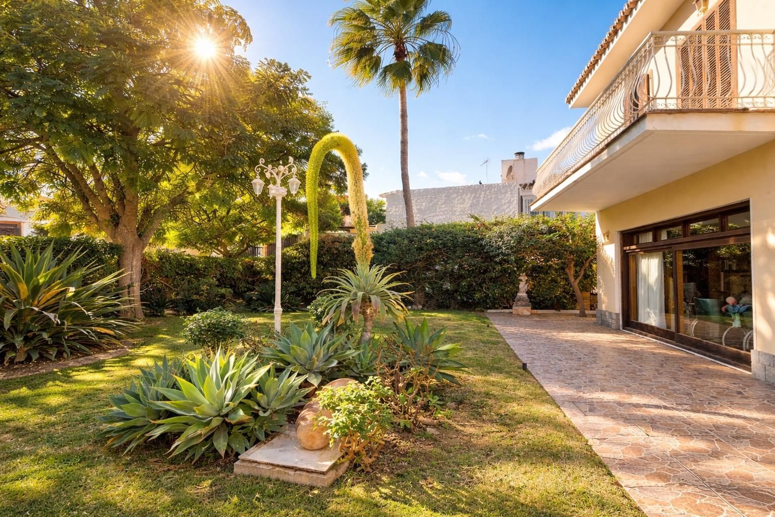 Casa beige de dos pisos con techo de tejas marrones y balcón bajo un cielo azul.