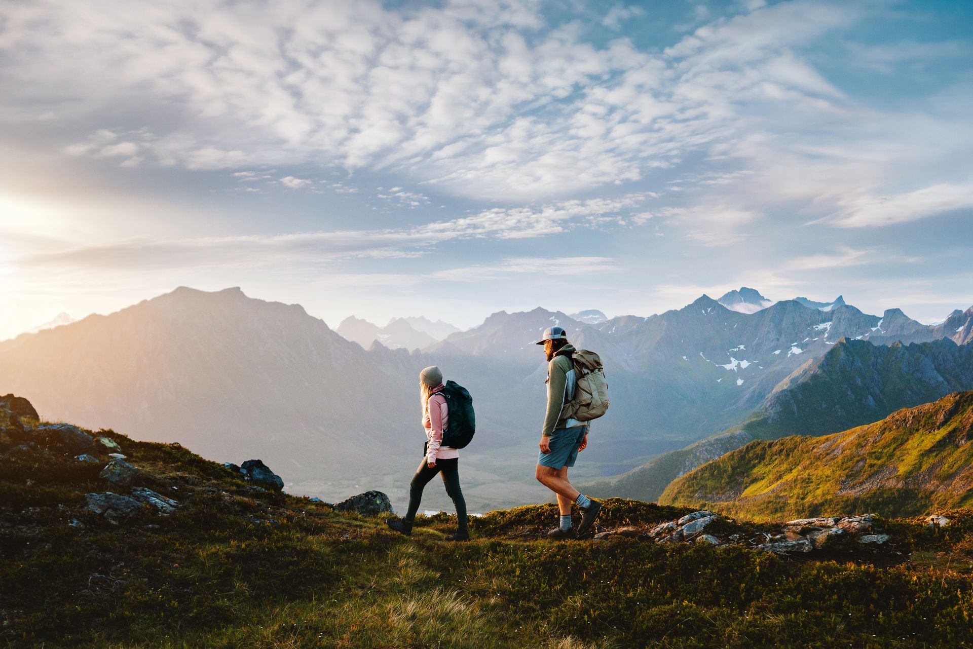 Deux randonneurs avec des sacs à dos marchant sur une crête montagneuse au lever du soleil.