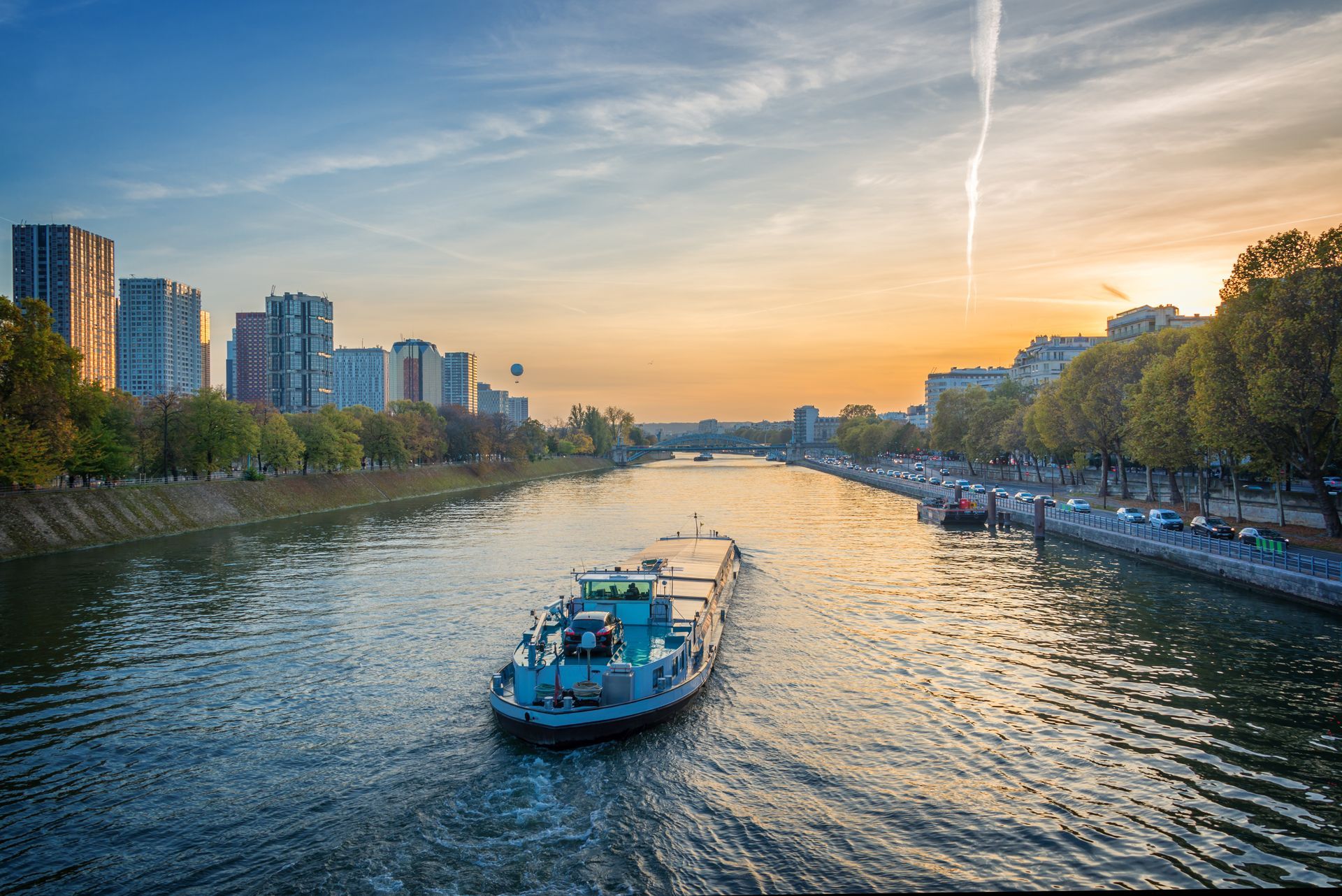 Vue du coucher de soleil depuis le pont d’un navire, sur un océan calme, avec un sol orange, une rambarde et une bouée de sauvetage.