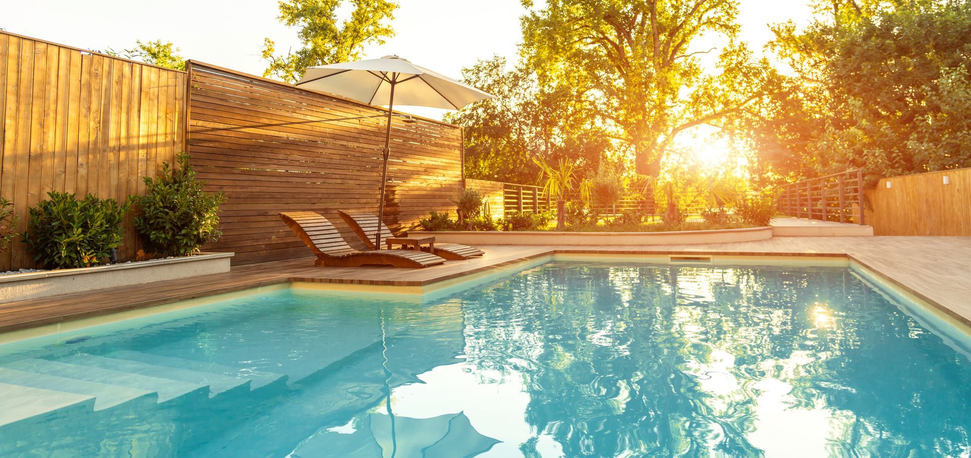 Piscine dans un jardin au coucher du soleil, avec des chaises longues baignées d’une douce lumière dorée.