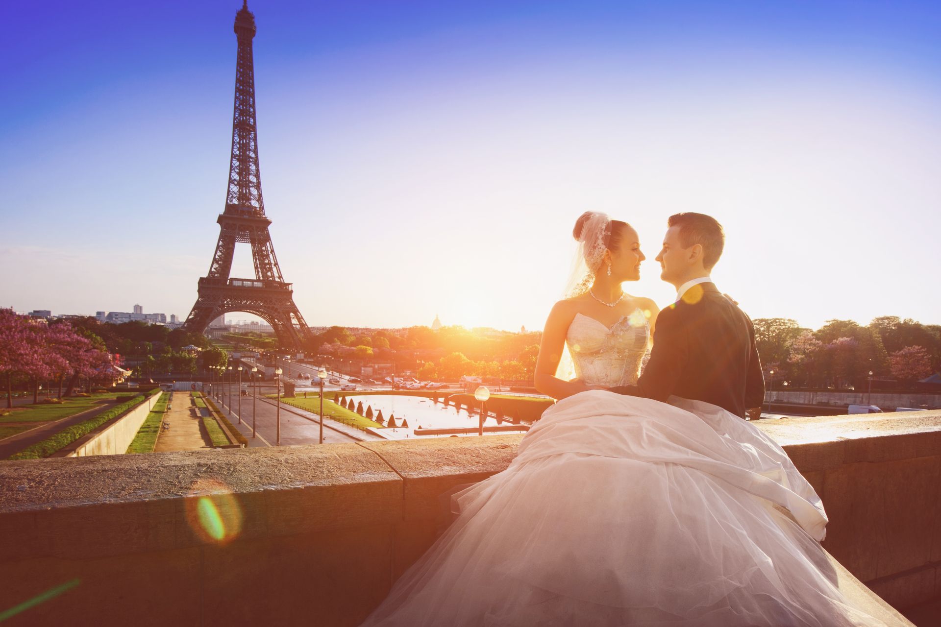 Un couple de mariés enlacé au coucher du soleil près de la tour Eiffel.