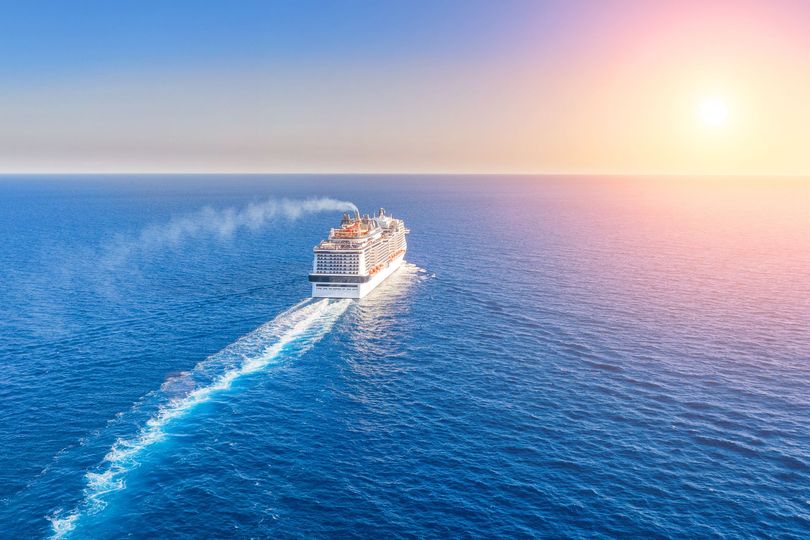 Un bateau de croisière navigue sur un océan bleu éclatant au coucher du soleil, laissant un sillage blanc derrière lui.