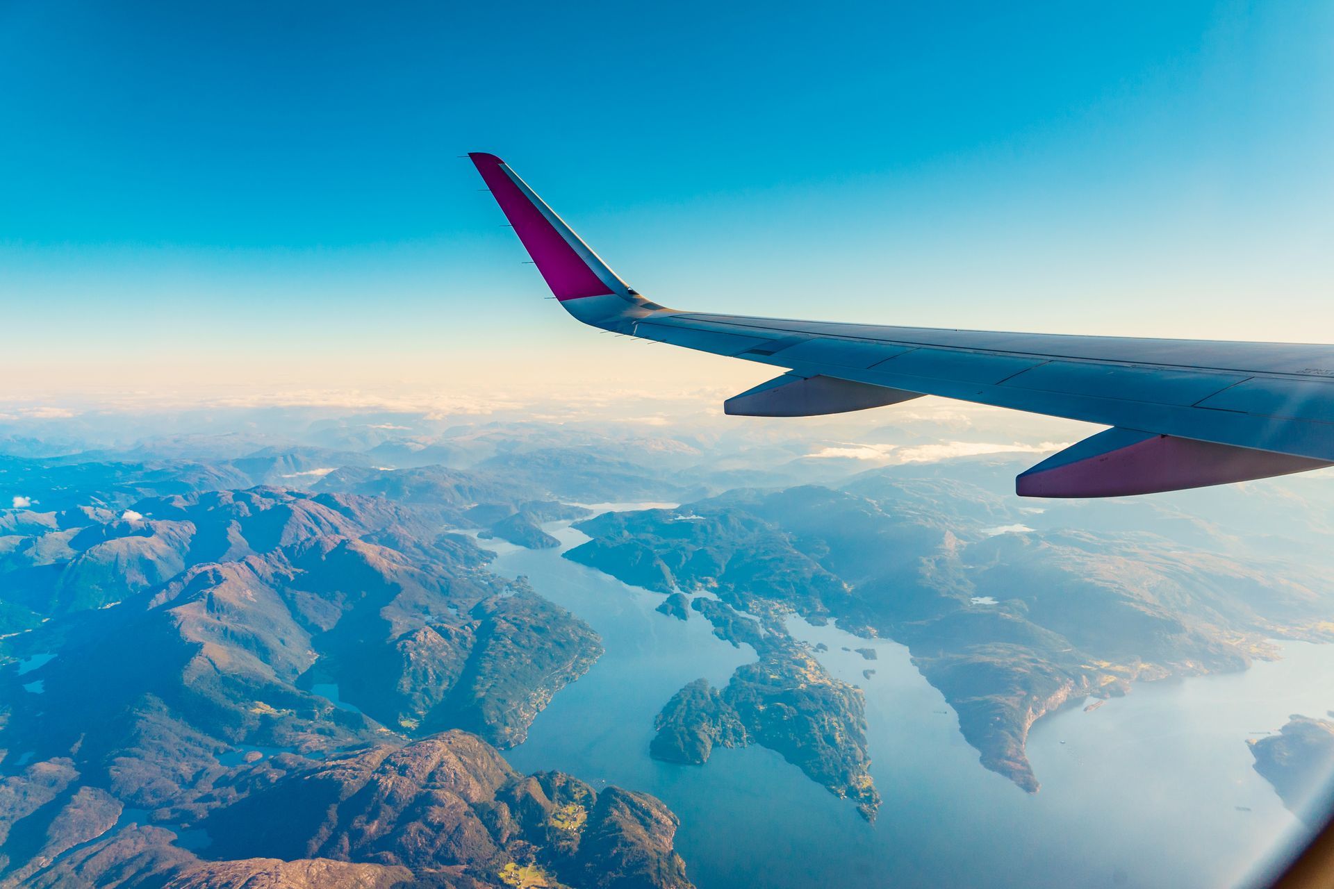 Aile d’avion au-dessus de montagnes et d’un lac, sous un ciel bleu dégagé.