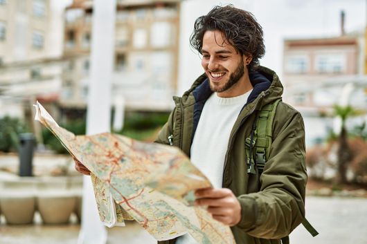 Homme souriant en veste verte lisant une carte papier en plein air.