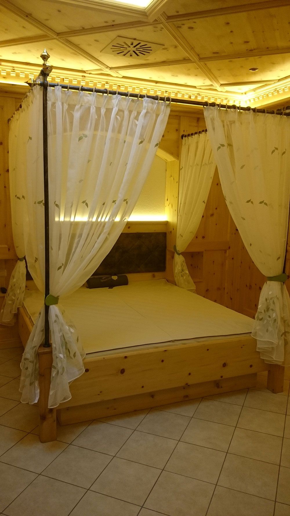 Ein Himmelbett aus Holz mit weißen Vorhängen in einem Schlafzimmer.