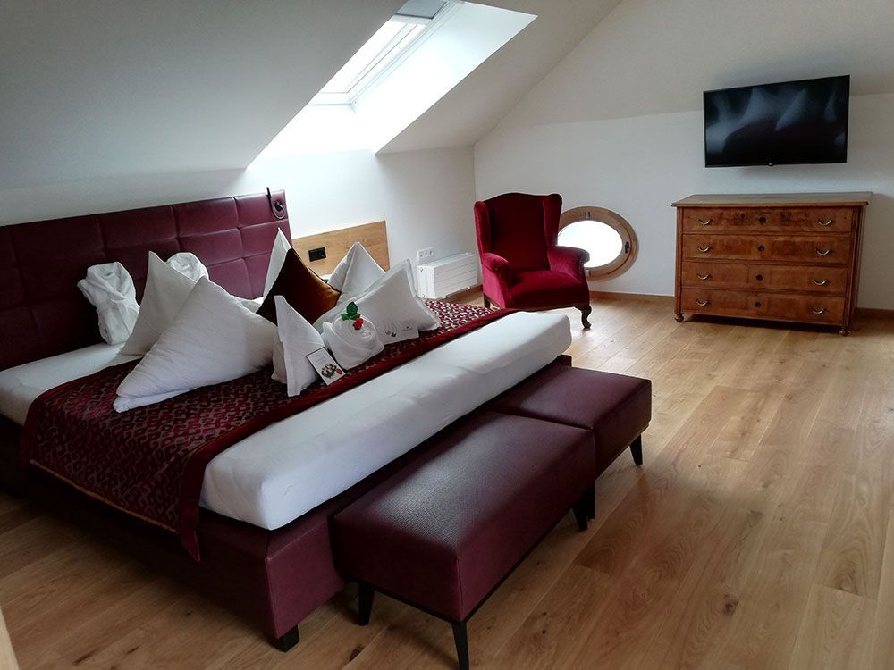 Ein Schlafzimmer mit großem Bett, Sessel, Kommode und Fernseher.