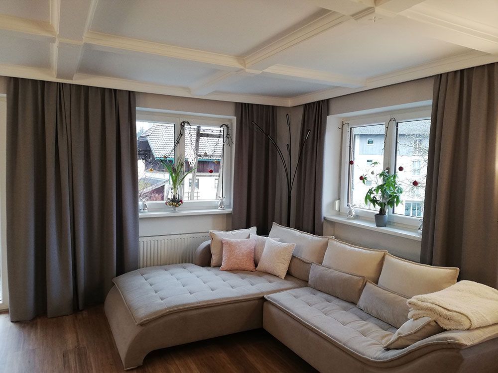 Ein Wohnzimmer mit großer Sofagarnitur und zwei Fenstern.